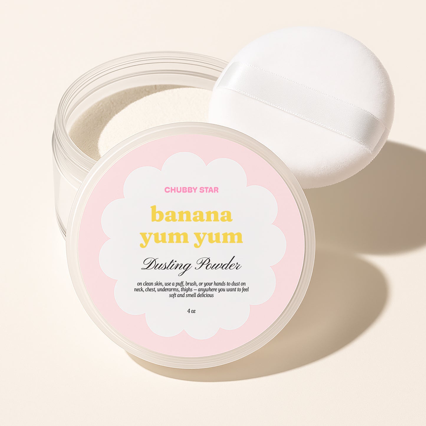Chubby Star Banana Yum Yum Dusting Powder in a clear jar with a white lid resting behind it, on a warm beige background.