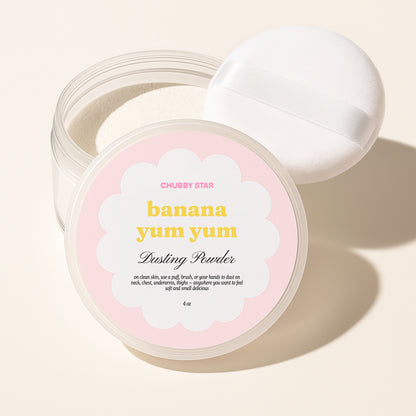 Chubby Star Banana Yum Yum Dusting Powder in a clear jar with a white lid resting behind it, on a warm beige background.