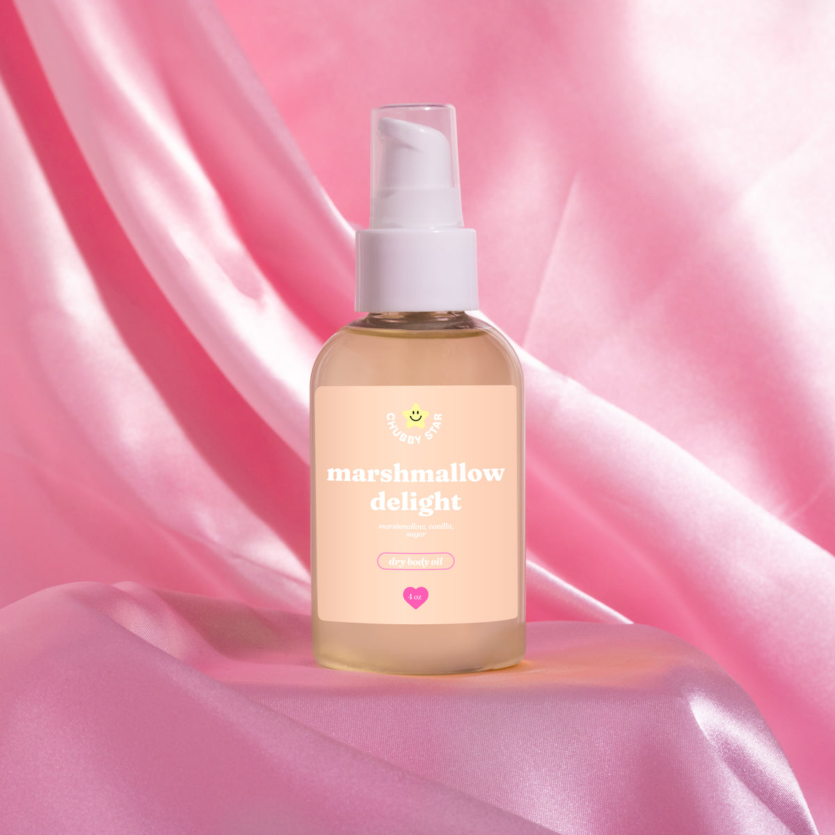 Bottle of 'marshmallow delight' scented body oil on a pink fabric background