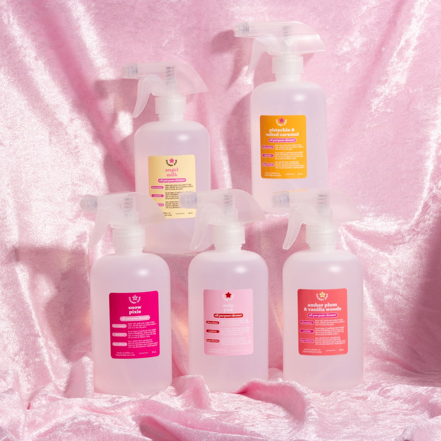 scented all purpose cleaning sprays are displayed in front of a pink velvet background for a trendy fun image. The scents shown are all different colors and smell like different dupes. There is one called Snow pixie, which is a dupe for lush snow fairy, Only You is a dupe for Glossier You, Amber Plum & Vanilla Woods is a dupe for the Brazilian Crush Cheirosa #40 scent, Pistachio & Salted Caramel is a dupe of the bum bum cream Cheirosa 62 scent, and Angel Milk is a dupe of the Lush Super Milk scent.