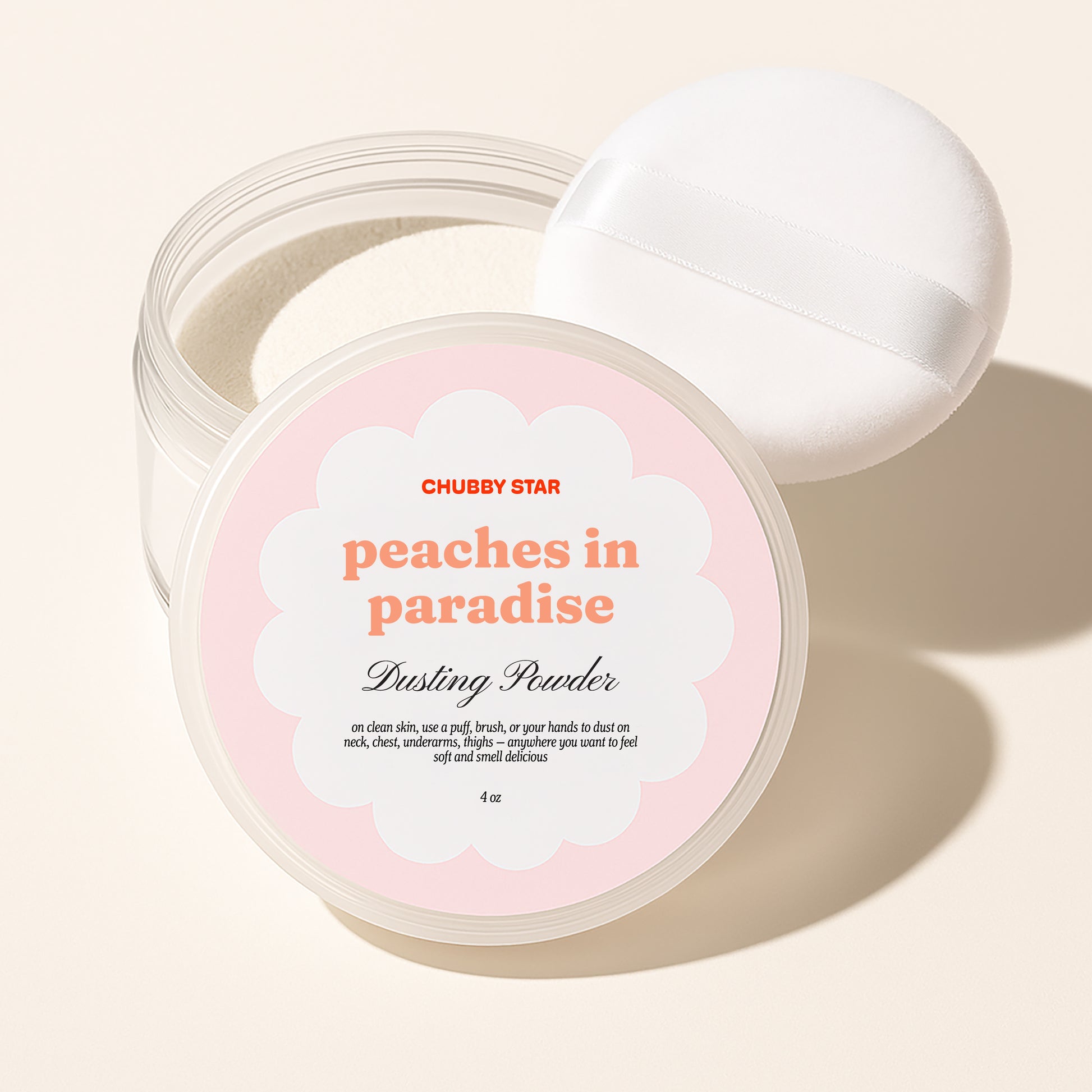 Chubby Star 'peaches in paradise,' a kayali eden sweet peach scented dusting powder in a clear jar with a white lid resting behind it, on a warm beige background.