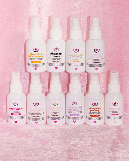 Row of white spray bottles with toilet mist spray product labels on a pink textured background