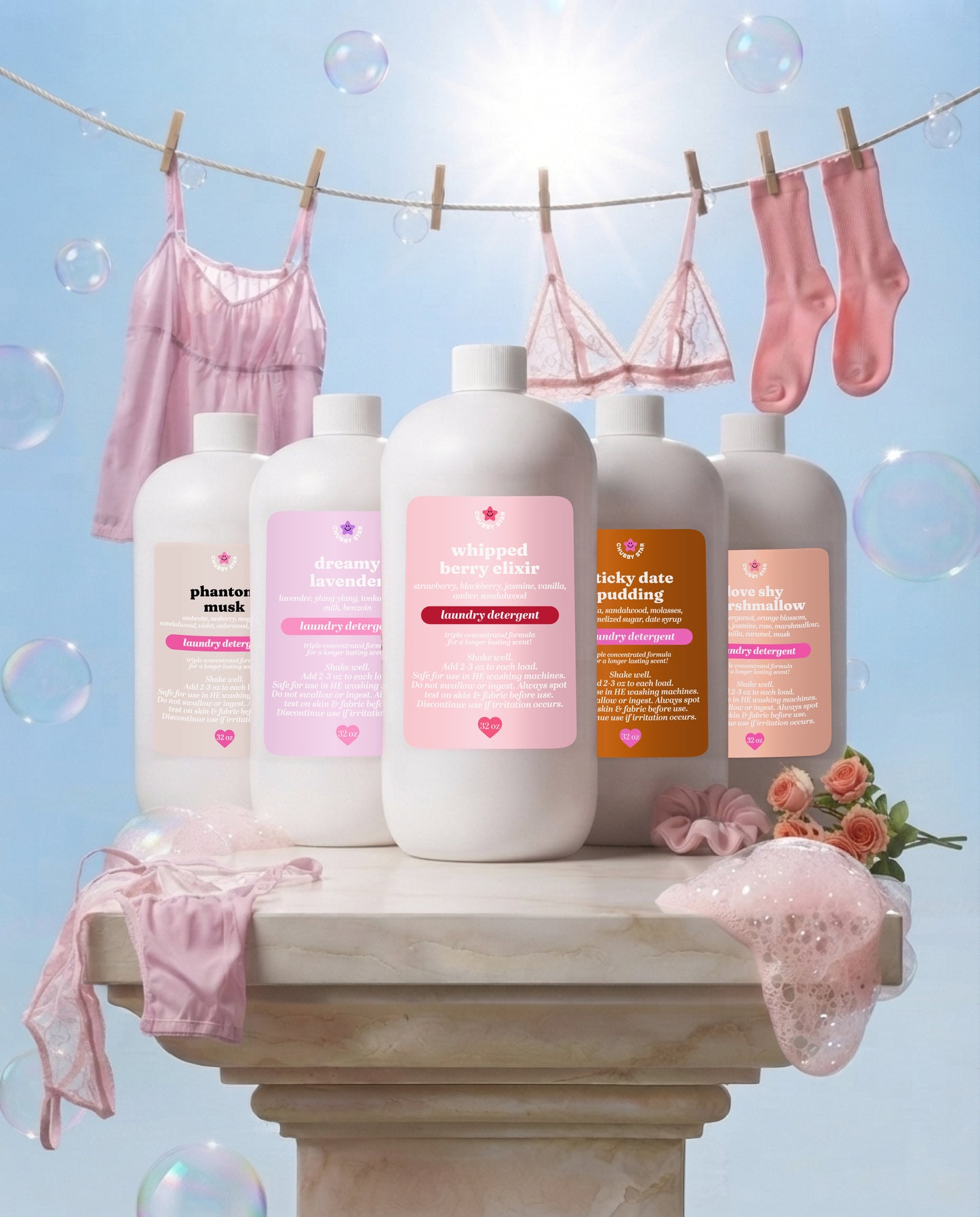 Five white laundry detergent bottles with pink and orange labels are arranged on a stone pedestal, surrounded by pink lingerie, socks, bubbles, and flowers against a bright blue sky background.