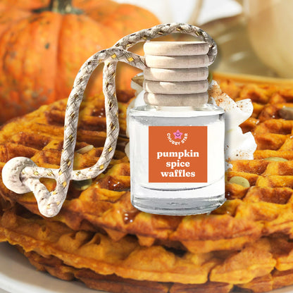 a glass bottle of pumpkin spice waffles scent as a car air freshener with an orange label on top of golden pumpkin waffles.