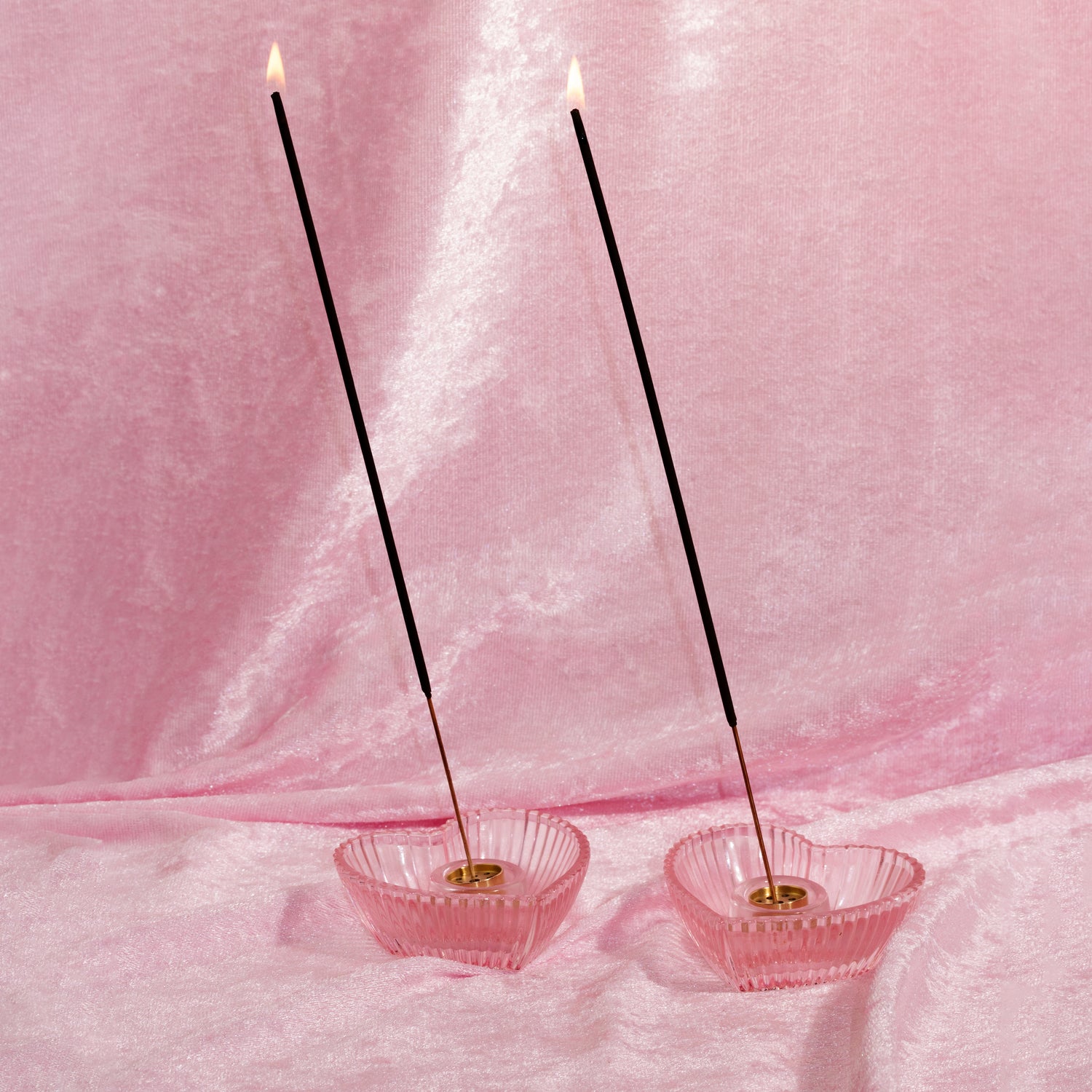 Two pink incense holders with lit scented incense sticks on a pink fabric background made by chubby star fragrances. The incense sticks smell like designer perfumes and are made with non toxic phthalate free fragrance oils
