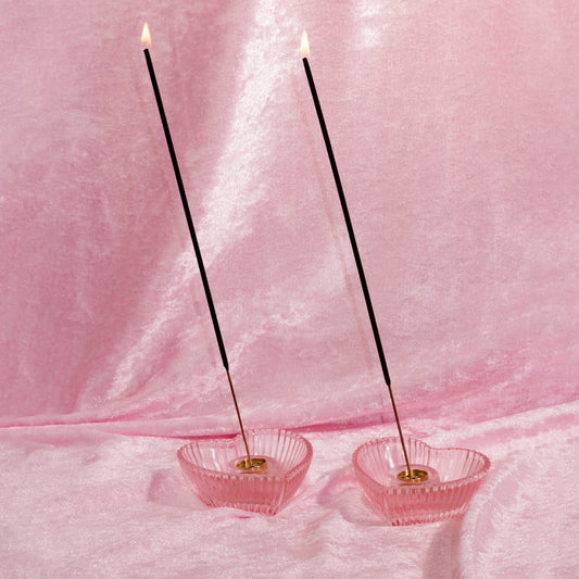 Two pink incense holders with lit scented incense sticks on a pink fabric background made by chubby star fragrances. The incense sticks smell like designer perfumes and are made with non toxic phthalate free fragrance oils