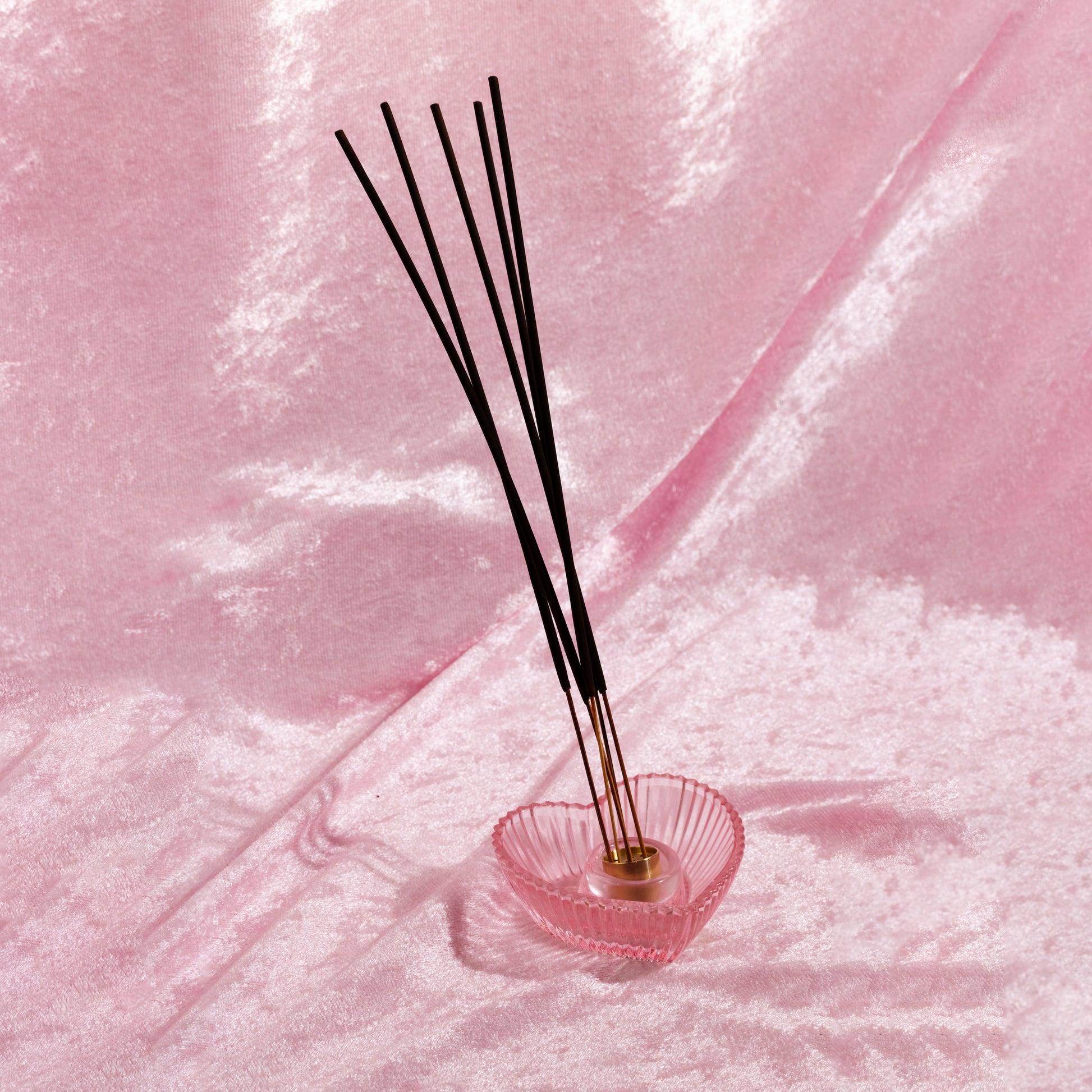 Heart-shaped incense holder with incense sticks on a pink velvet background. Incense sticks smell like designer dupe fragrances, made by Chubby Star in the USA